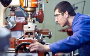 Ein junger Mann mit blauer Kleidung schaut auf einen Industrie-Bohrer