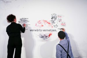 Zwei Personen zeichnen auf eine weiße Wand im Comic-Stil und einigen Begrifflichkeiten